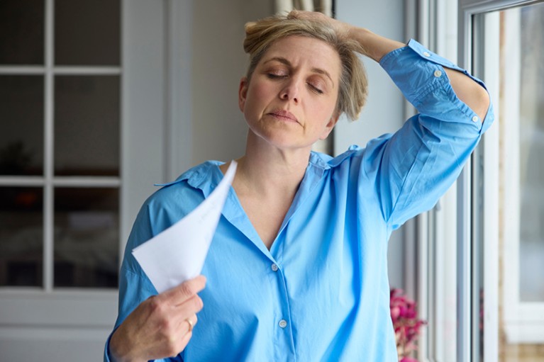 Menopausal Mature Woman Having Hot Flush At Home Cooling Herself With Letters Or Documents; Shutterstock ID 2281774401; purchase_order: -; job: -; client: -; other: -
